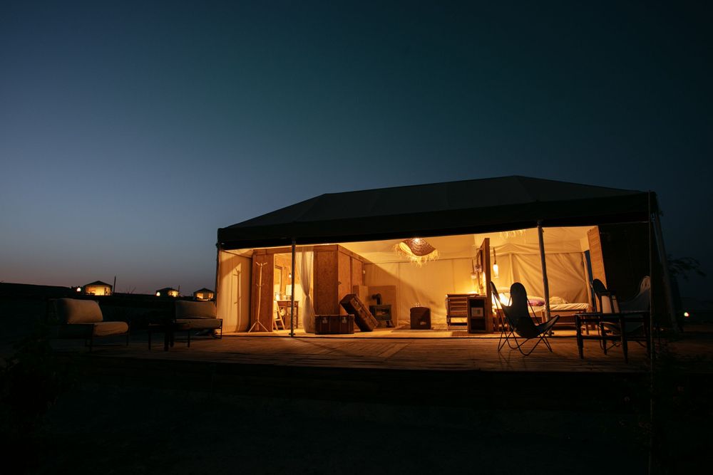 Modern illuminated glamping tent at dusk with warm interior lighting.