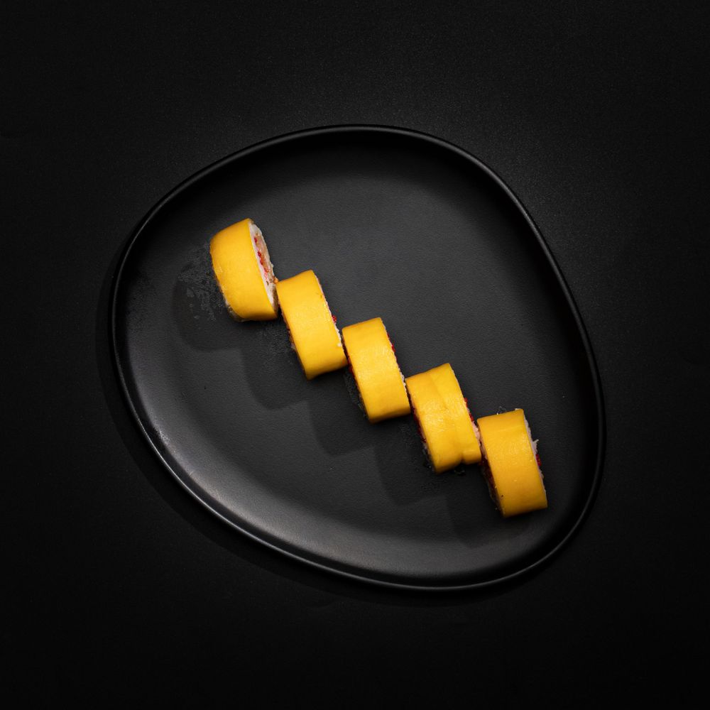 Sliced yellow mango arranged diagonally on black ceramic plate.