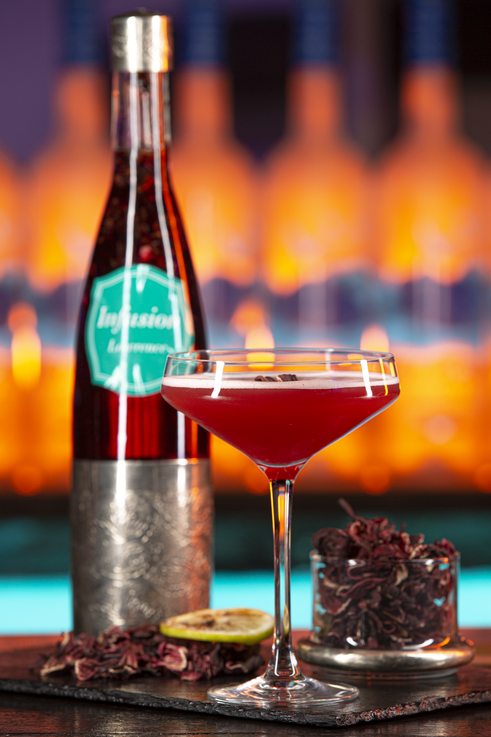 Elegant cocktail in martini glass with bottle and garnishes on dark bar setting.