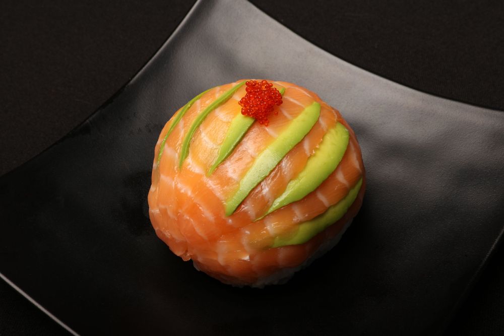 Artistic sushi roll with salmon and avocado slices on black plate.