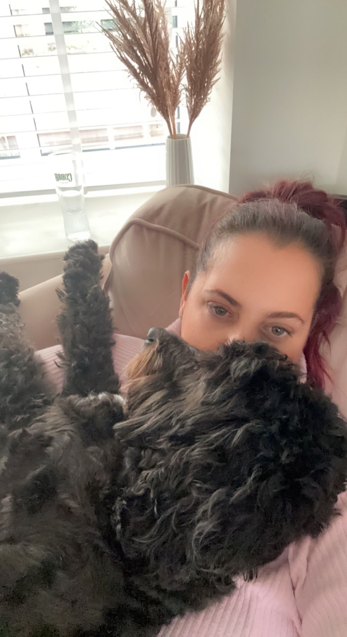 Person takes selfies with a fluffy black dog on a pink couch.