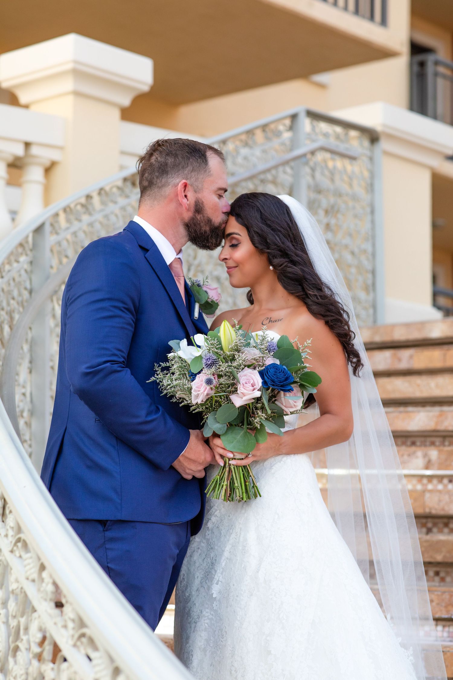 A romantic wedding portrait on elegant stone stairs featuring a beautiful bouquet of mixed flowers.