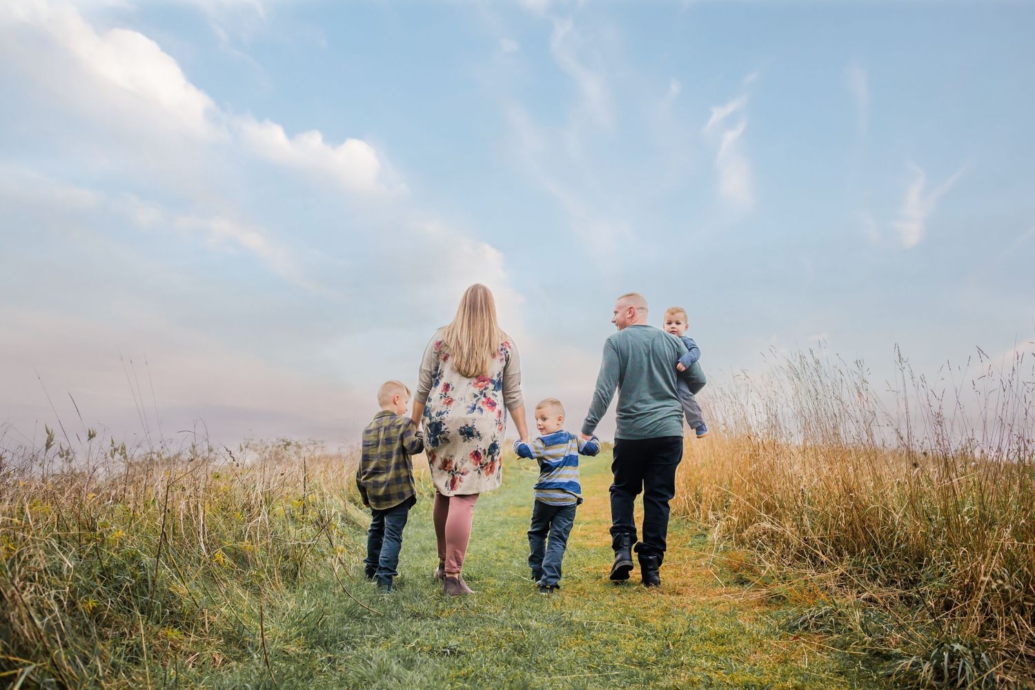 Family walking together holding hands on nature trail against sky at sunset.