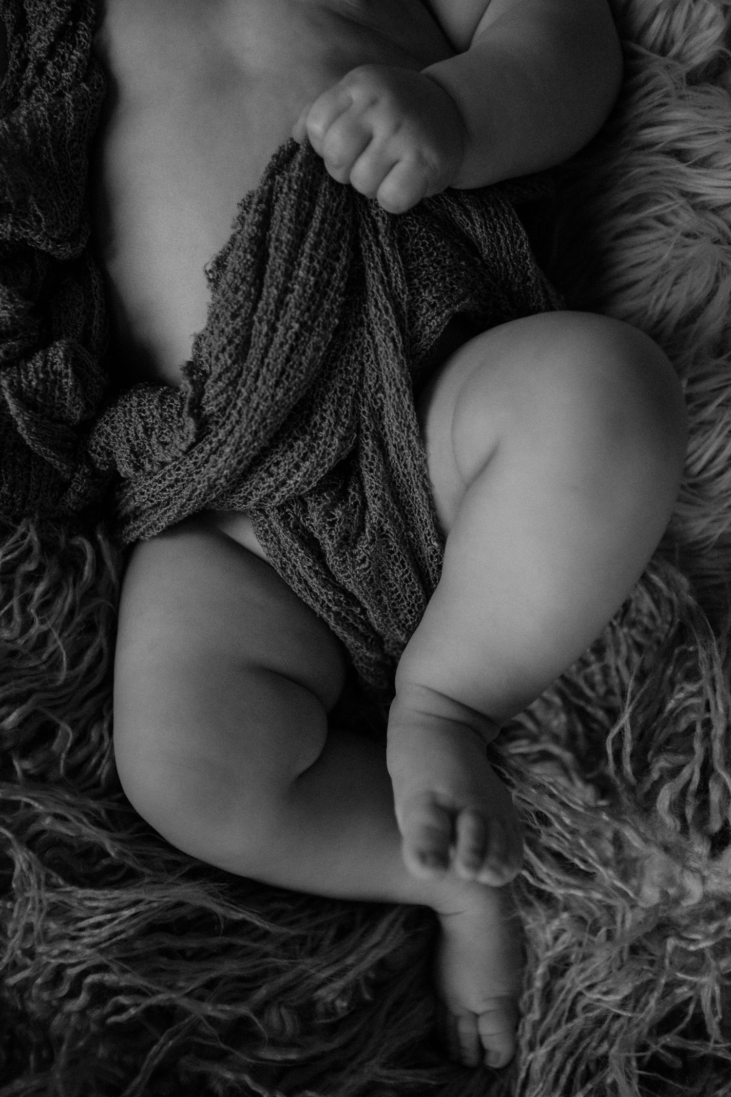 Black and white close-up of newborn baby legs wrapped in knit blanket on fur.