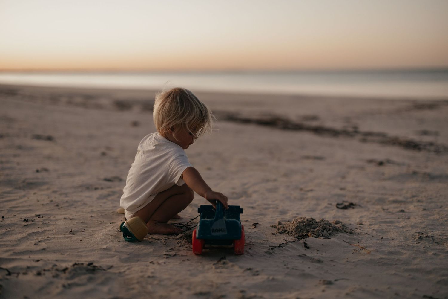 Young child playing with a blue toy on sandy beach at sunset.