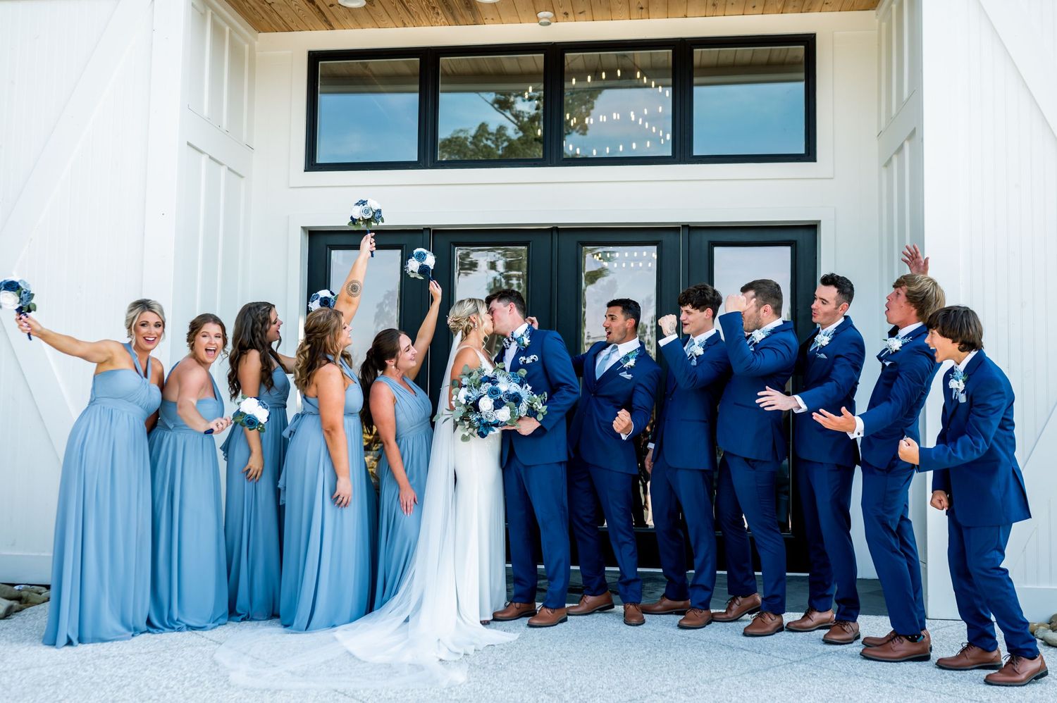 Wedding party in navy and light blue attire poses together outside modern venue.