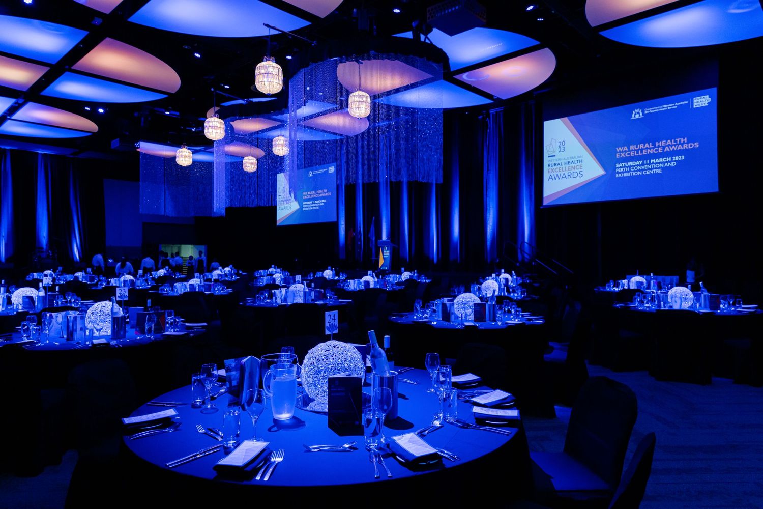 Elegant ballroom setup with blue lighting and round tables for a corporate event or gala.