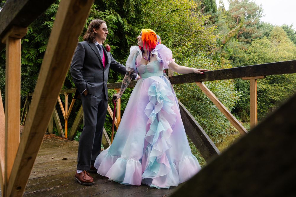 Eliza and Michael in their rainbow wedding attire and suit on a bridge at Brookfield Barn