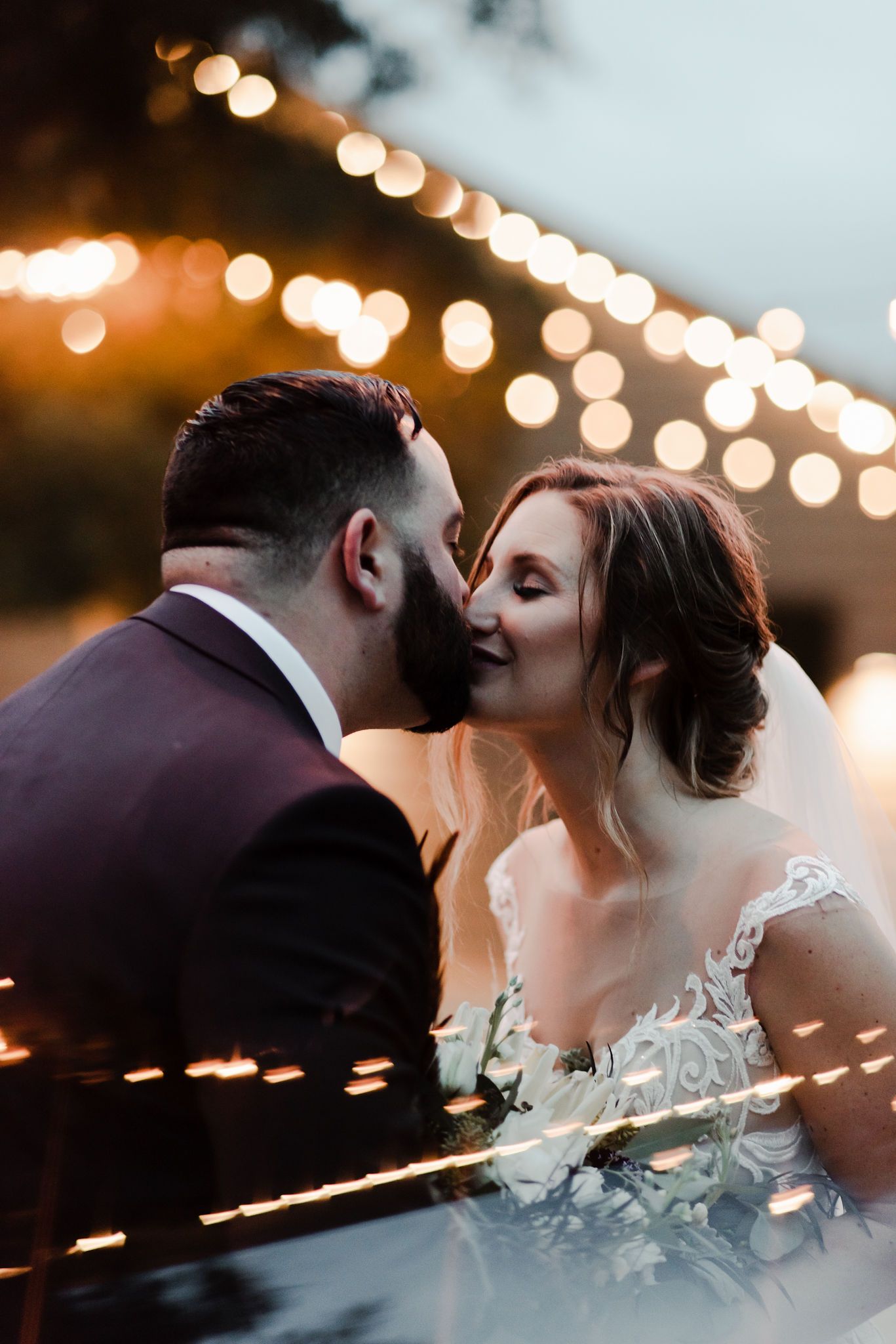 Close up of bride and groom kissing at twilight surrounded by glowing romantic twinkle light bokeh