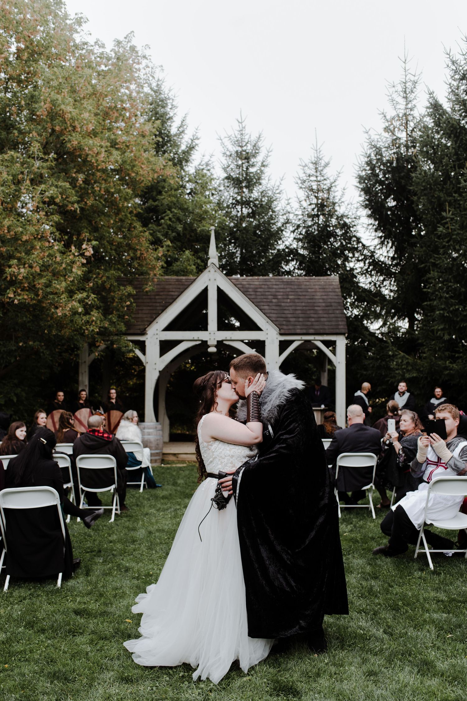 Bride and groom in medieval wedding attire kiss at the end of their ceremony aisle