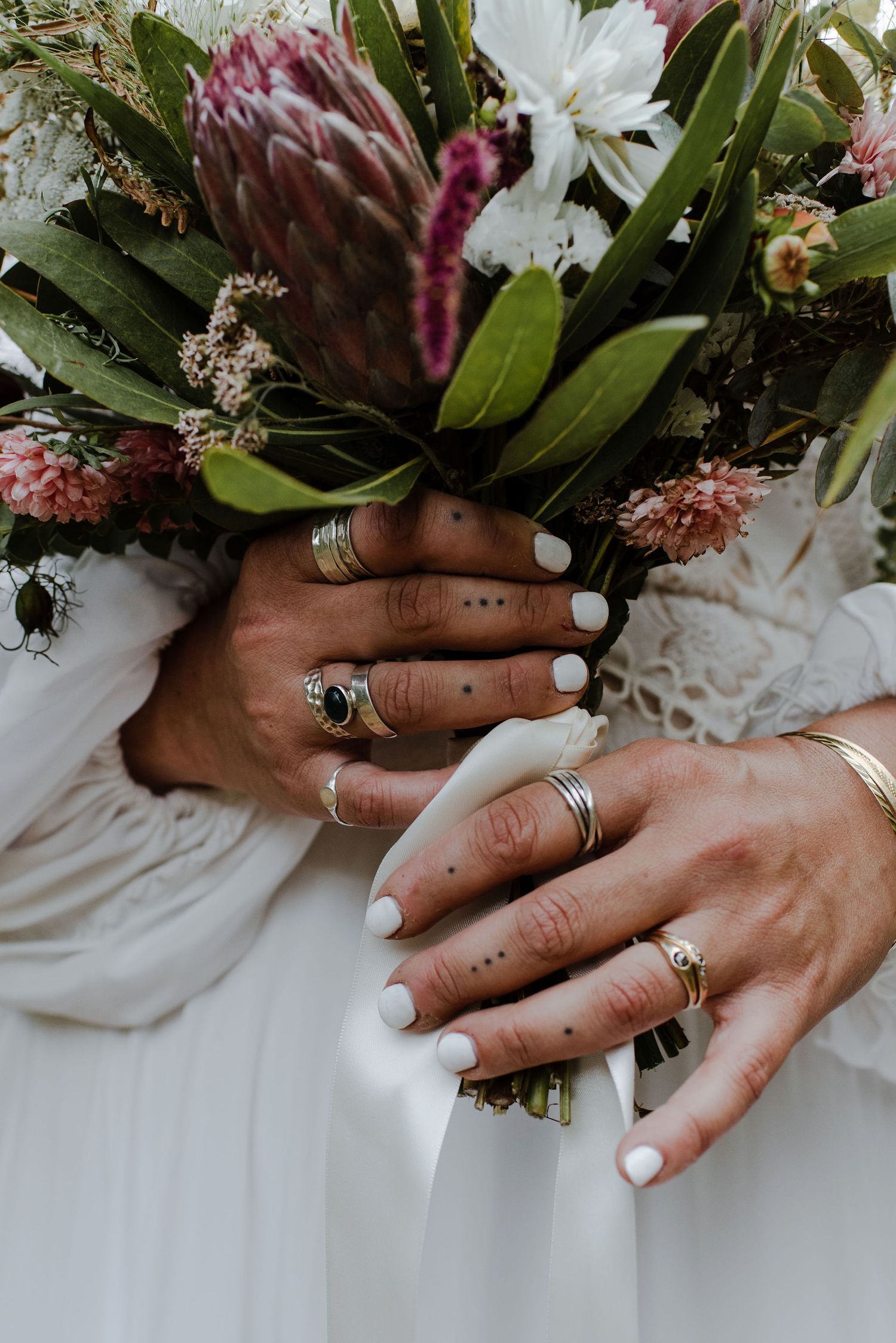 Close up of a bride's tattooed fingers and eclectic rings as she holds her bouquet at her waist