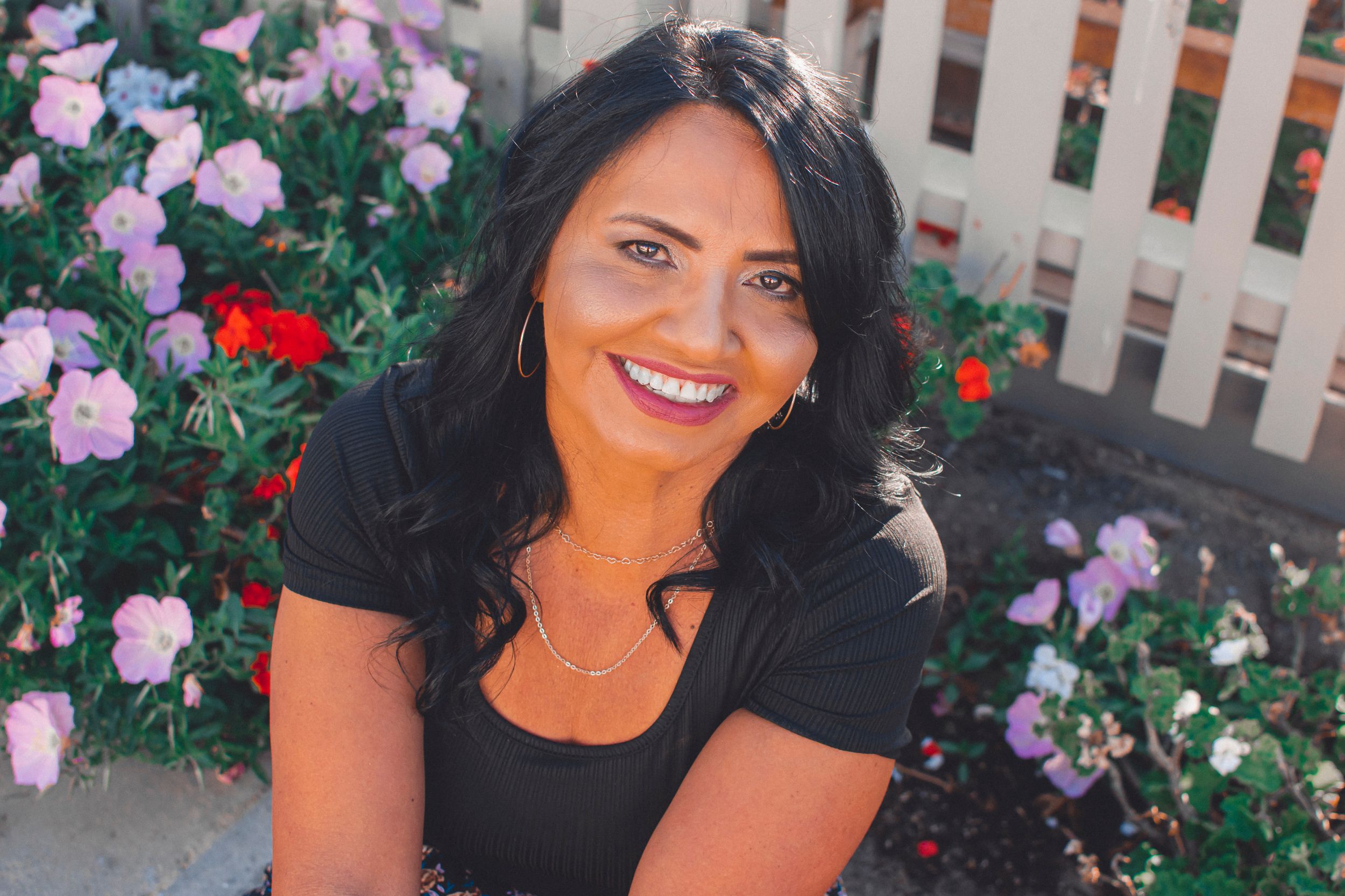 A sunny outdoor portrait surrounded by pink and red roses against a white picket fence.