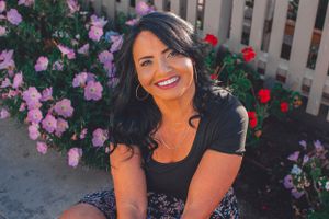 A casual outdoor portrait among blooming pink and red roses by a wooden fence.