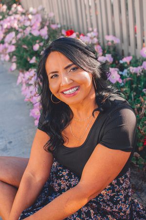 A bright outdoor portrait with pink roses and a white picket fence in the background.