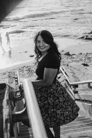 A casual seaside photoshoot featuring someone on wooden steps with ocean waves in the background.