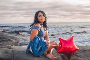 Relaxed beachside portraits with a red star pillow prop on rocky coastline.