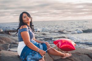 Casual seaside photography session with denim and red accents against ocean backdrop.