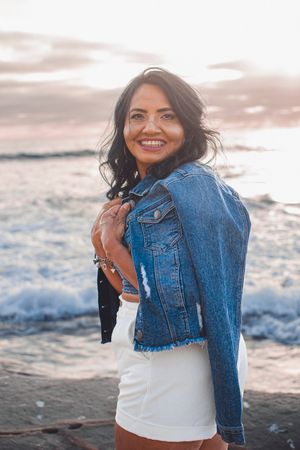 Lifestyle photos showing genuine smiles and laughter while modeling denim jacket on beach at golden hour.