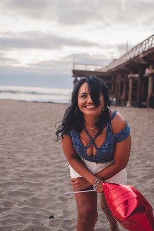 Candid moments during beach photoshoot with blue top and red balloon near oceanside pier.