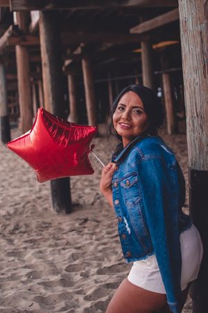 Casual beach portrait with denim jacket and red star balloon under wooden pier.