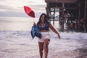 Playful moment splashing in ocean waves while holding red star balloon near pier.