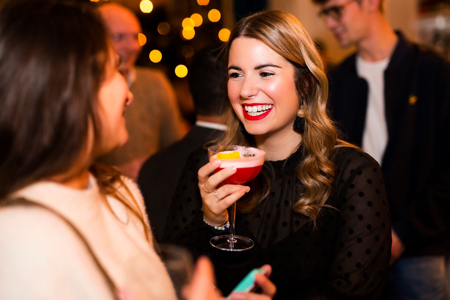 A social gathering at night with cocktails and bokeh lighting in the background.