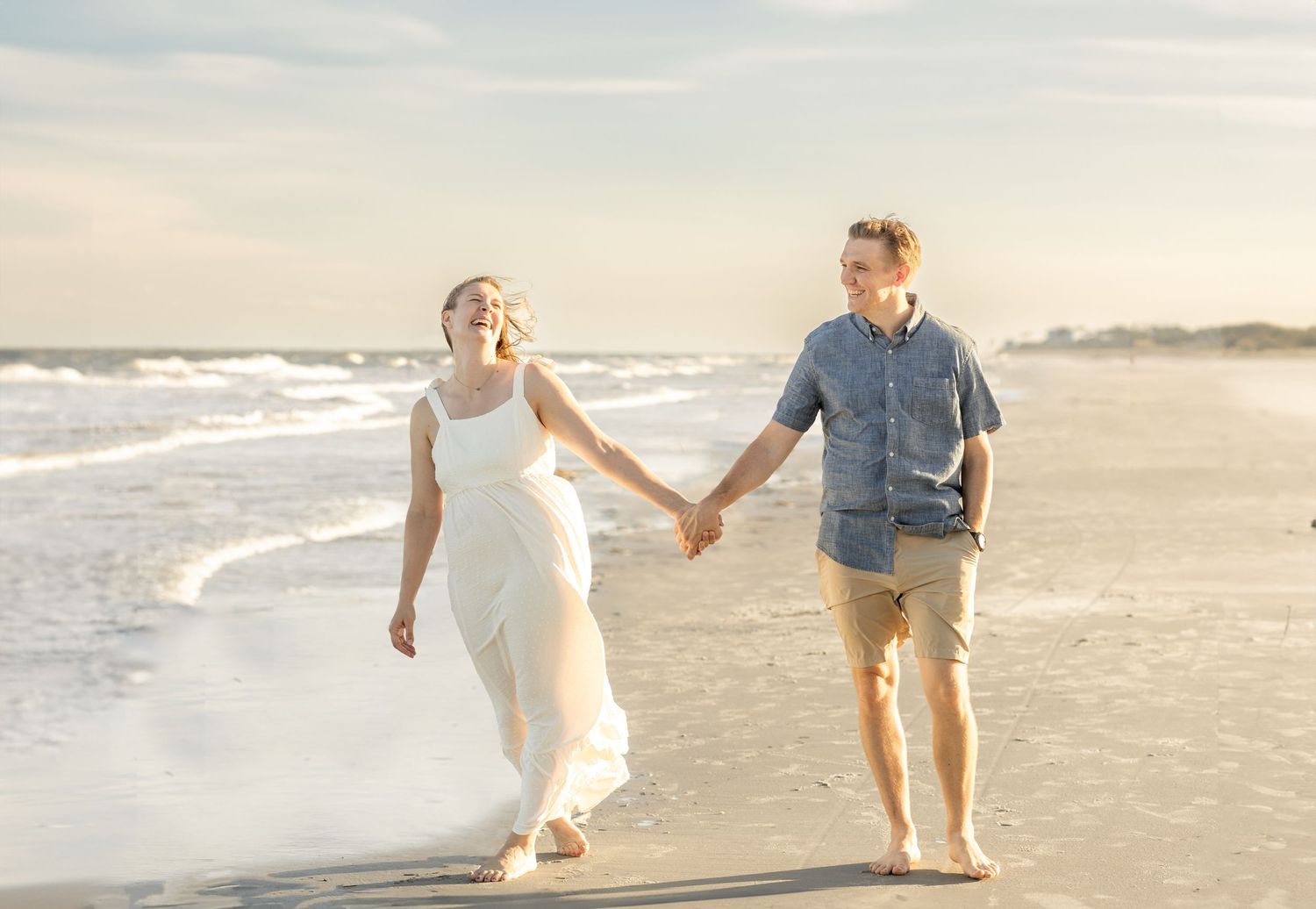 Romantic beach photoshoot of couple holding hands while walking by the ocean.