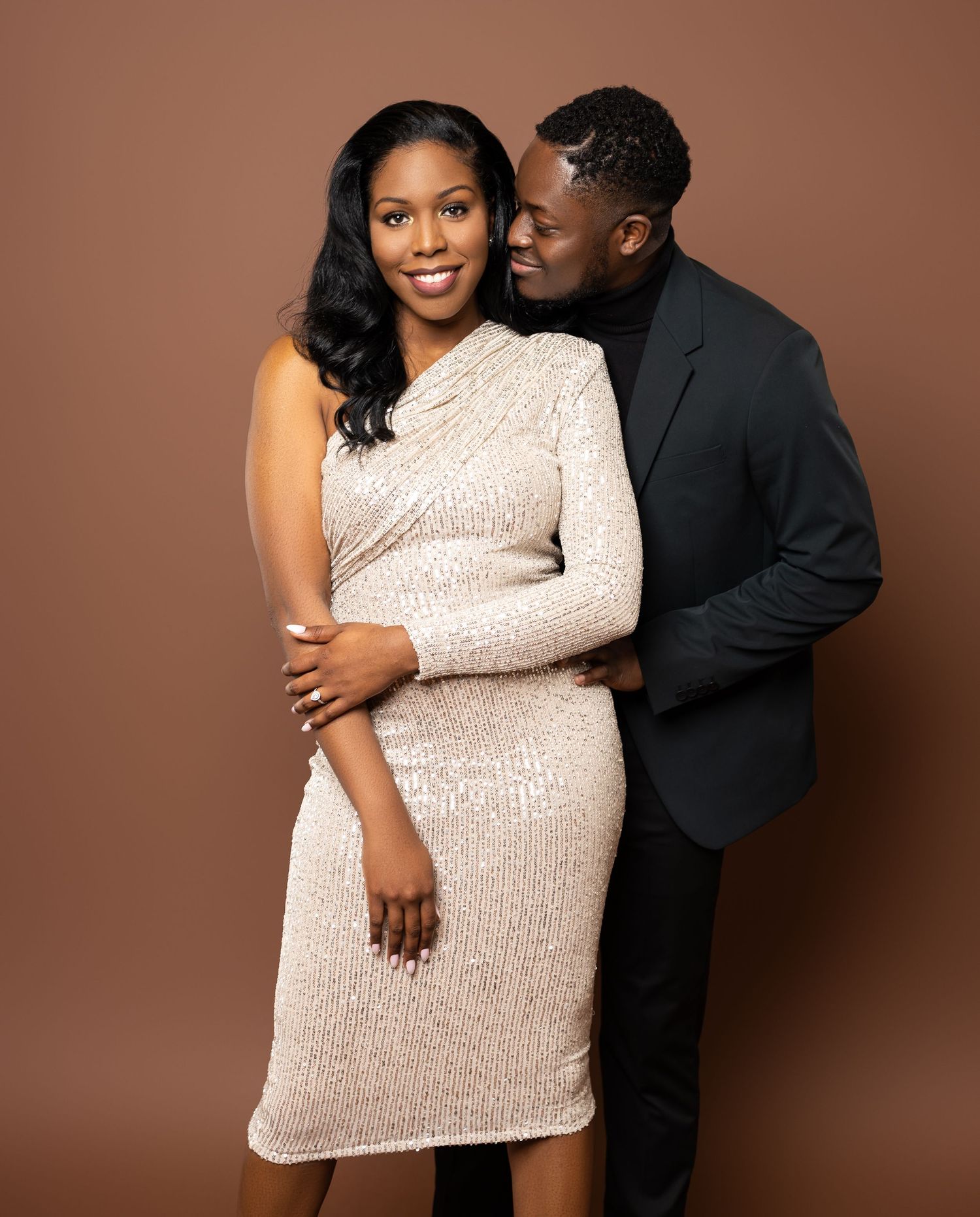 Romantic couple poses in formal wear with white sequined dress and black blazer in studio portrait.