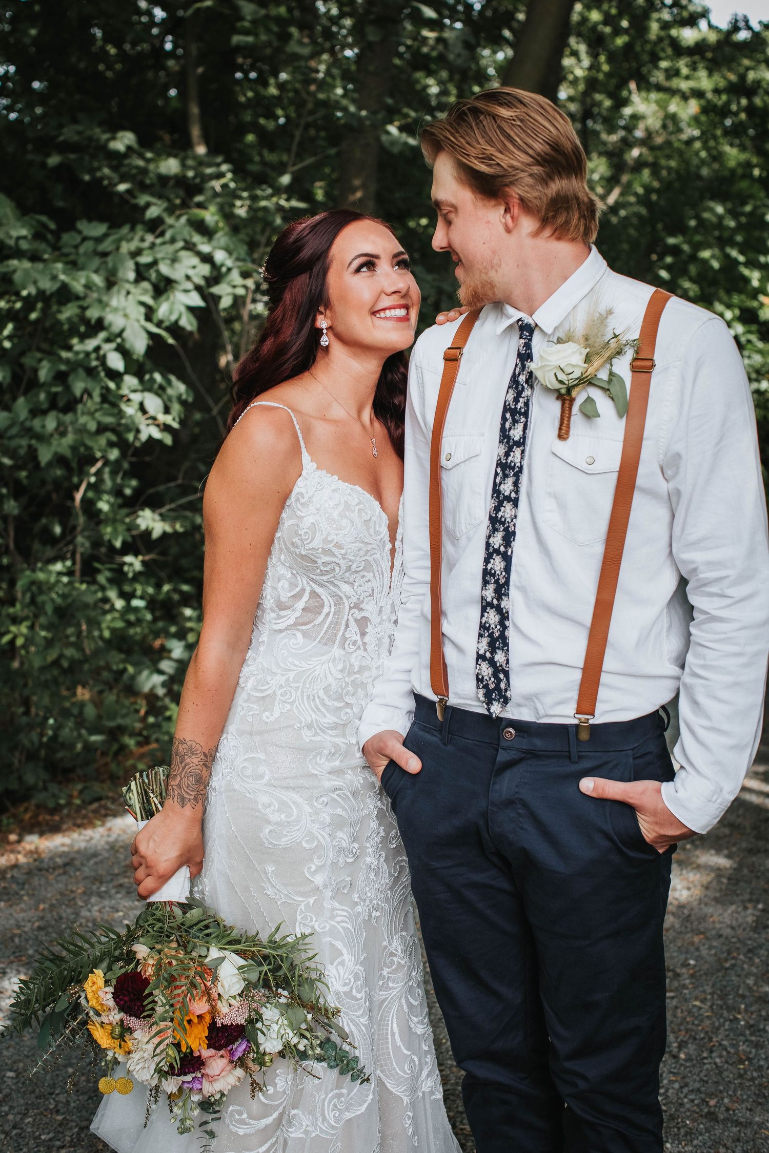 A romantic wedding couple in rustic attire share a moment outdoors.