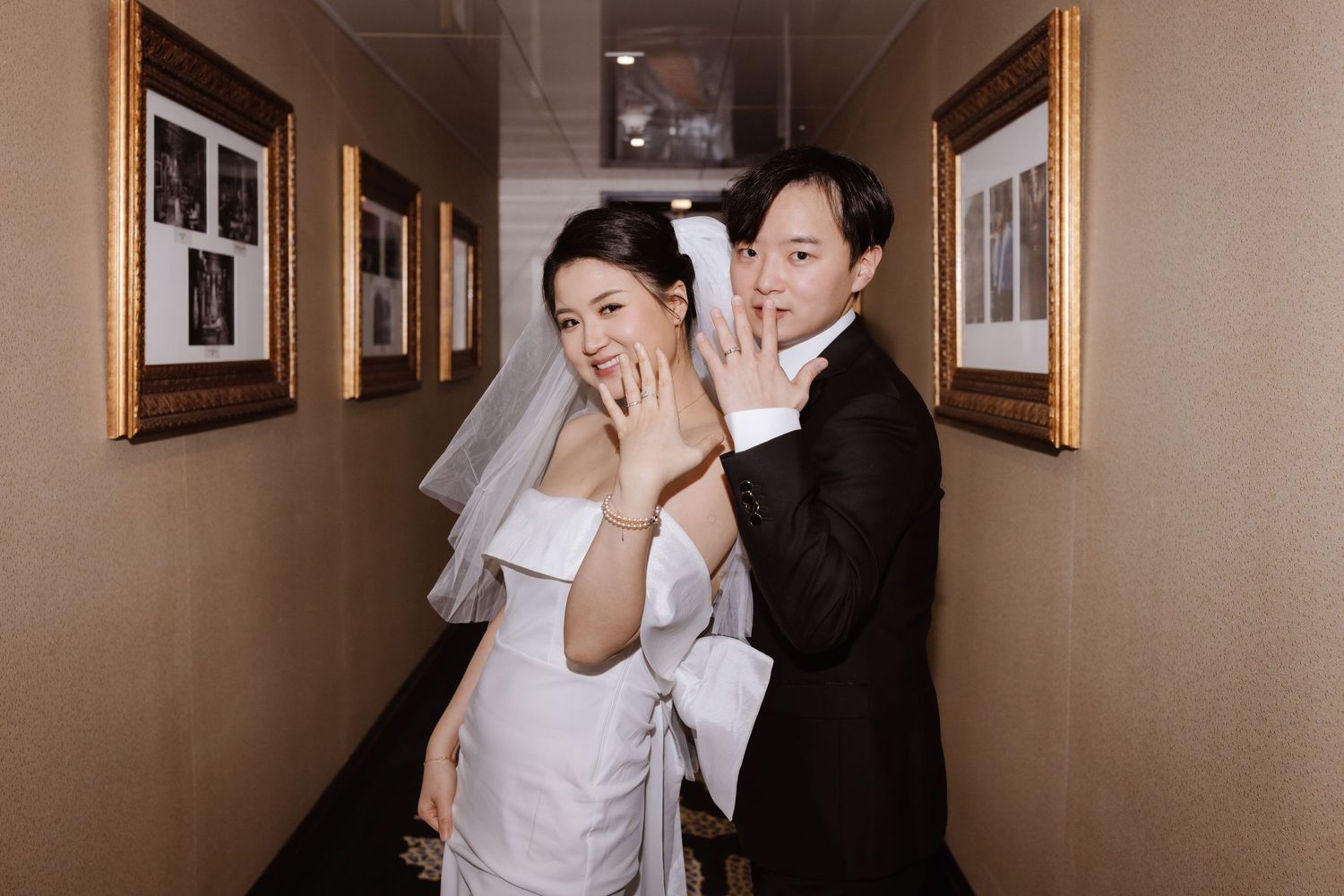 Playful wedding moment captured in hotel hallway with gold-framed artwork.