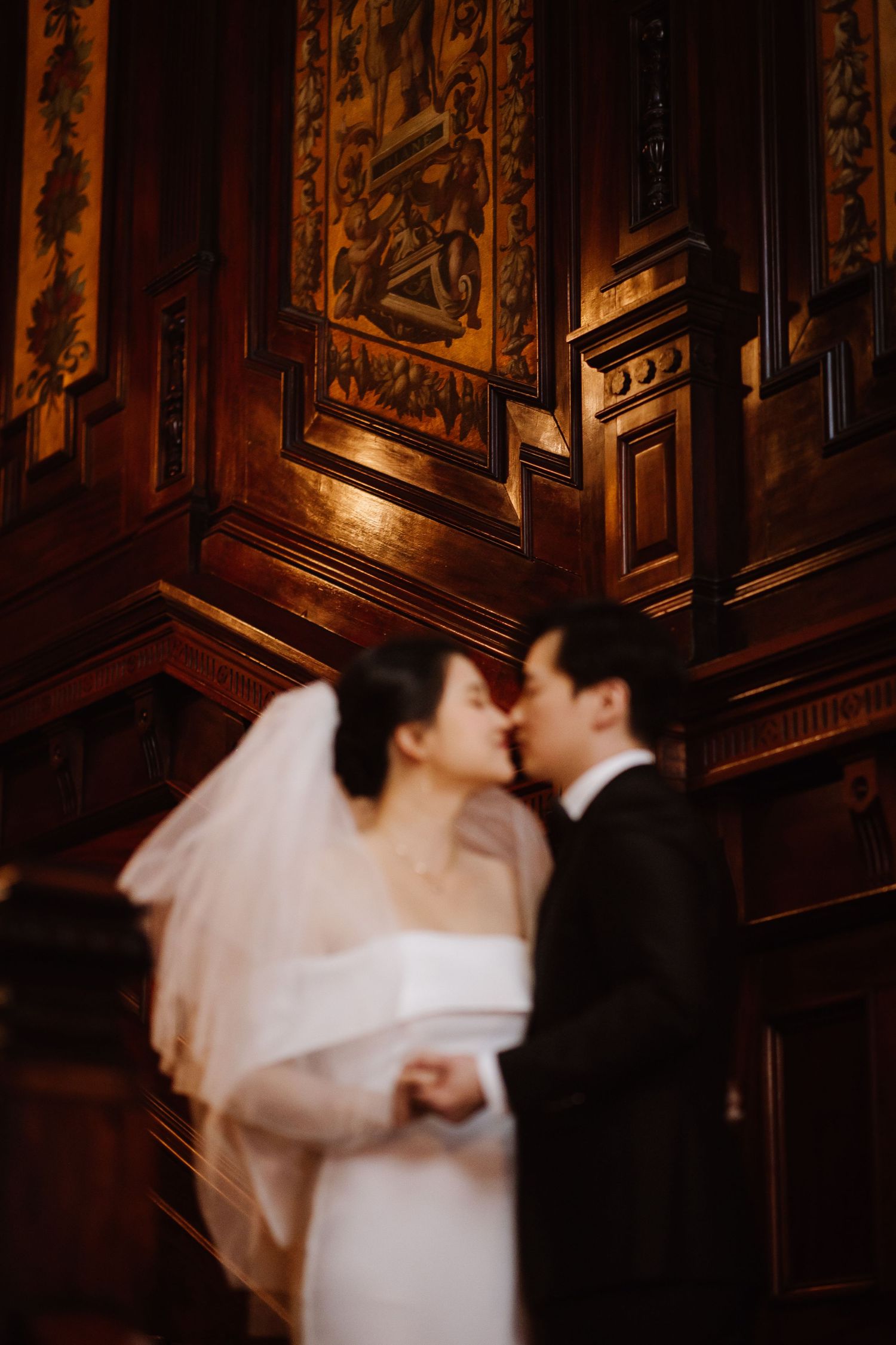 Intimate wedding kiss captured against backdrop of ornate wooden wall panels.