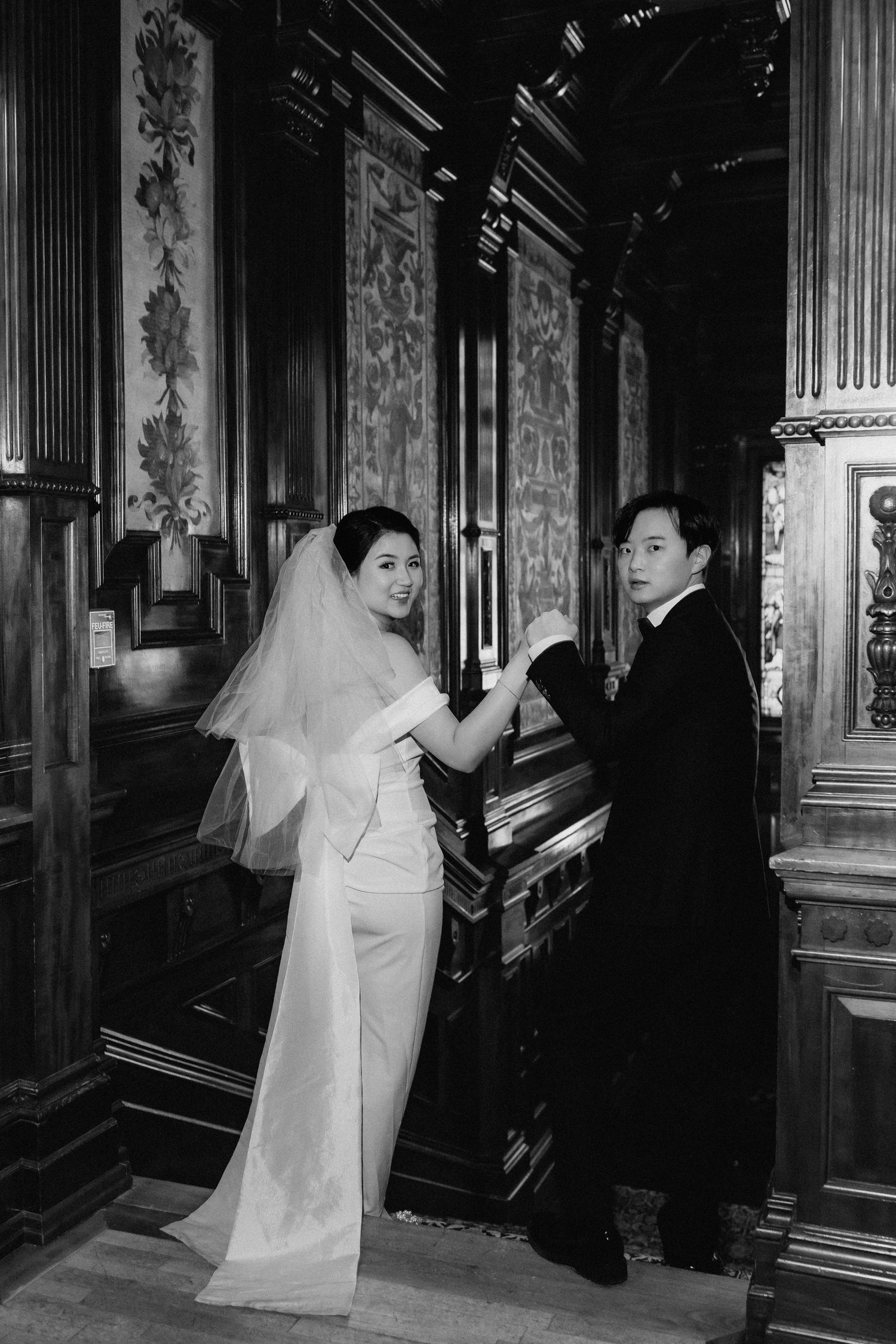Black and white wedding photo of couple by decorative wood panels in classic venue.