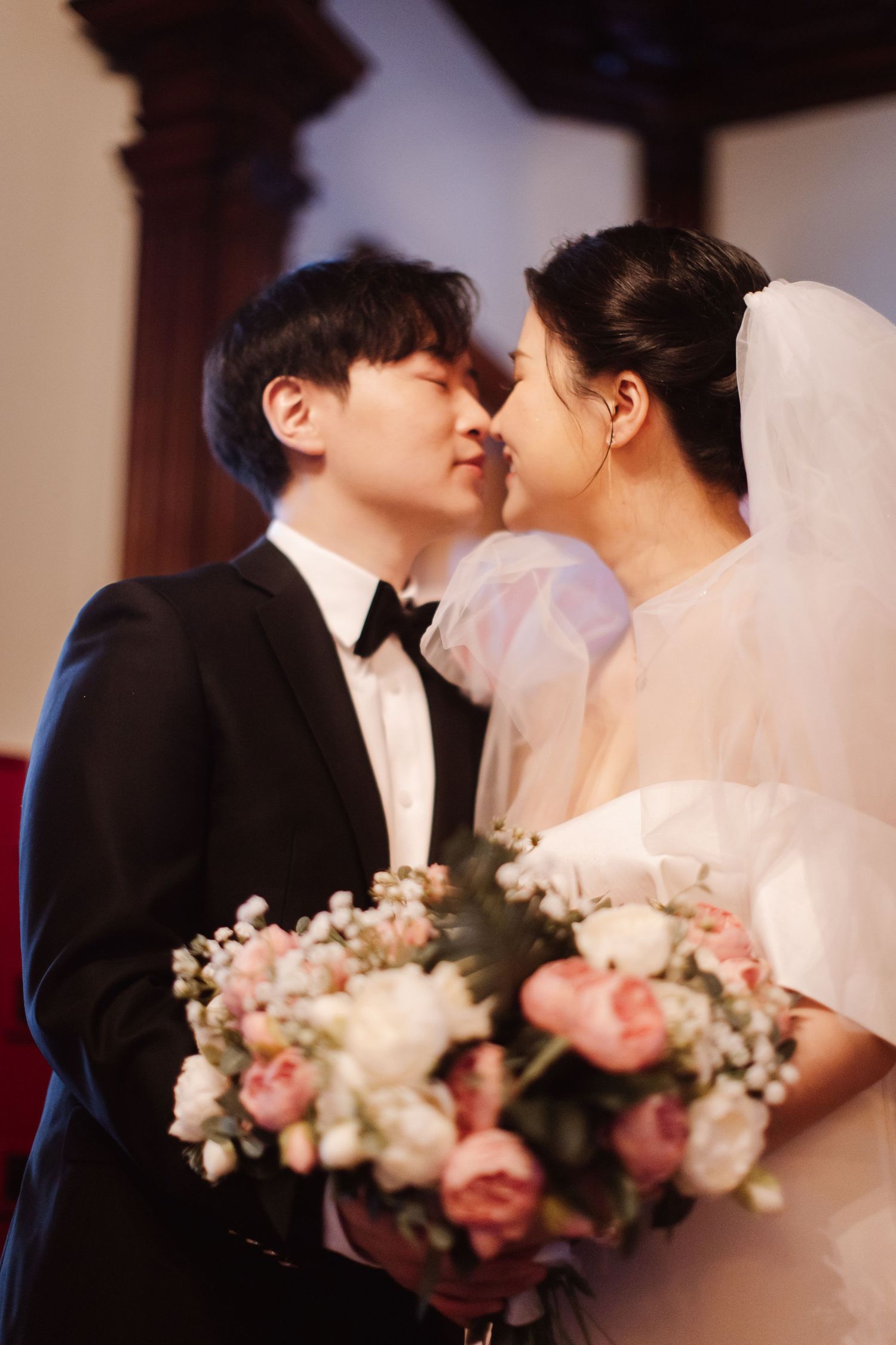 Romantic wedding moment with couple sharing kiss as bride holds pink floral bouquet.