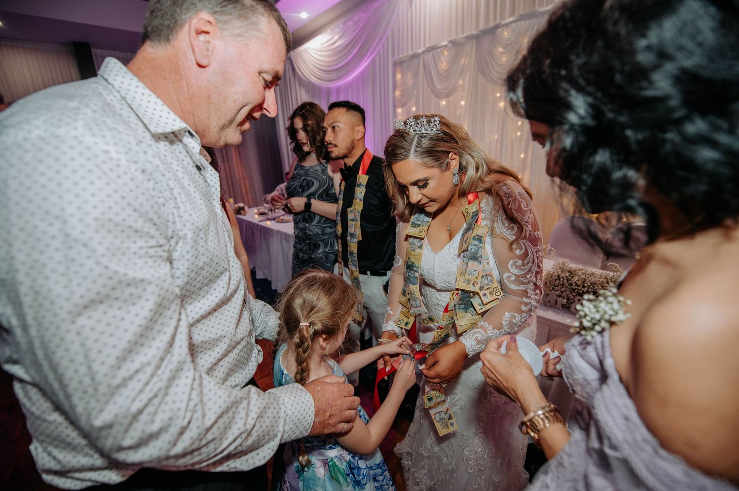 Wedding guests gather around to interact with children during reception celebration.