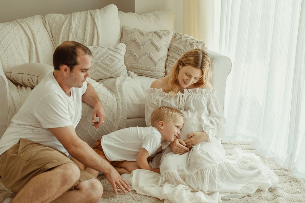 Family intimacy portrayed in an airy studio, with parents and a toddler focused on the soon-to-arrive baby bump