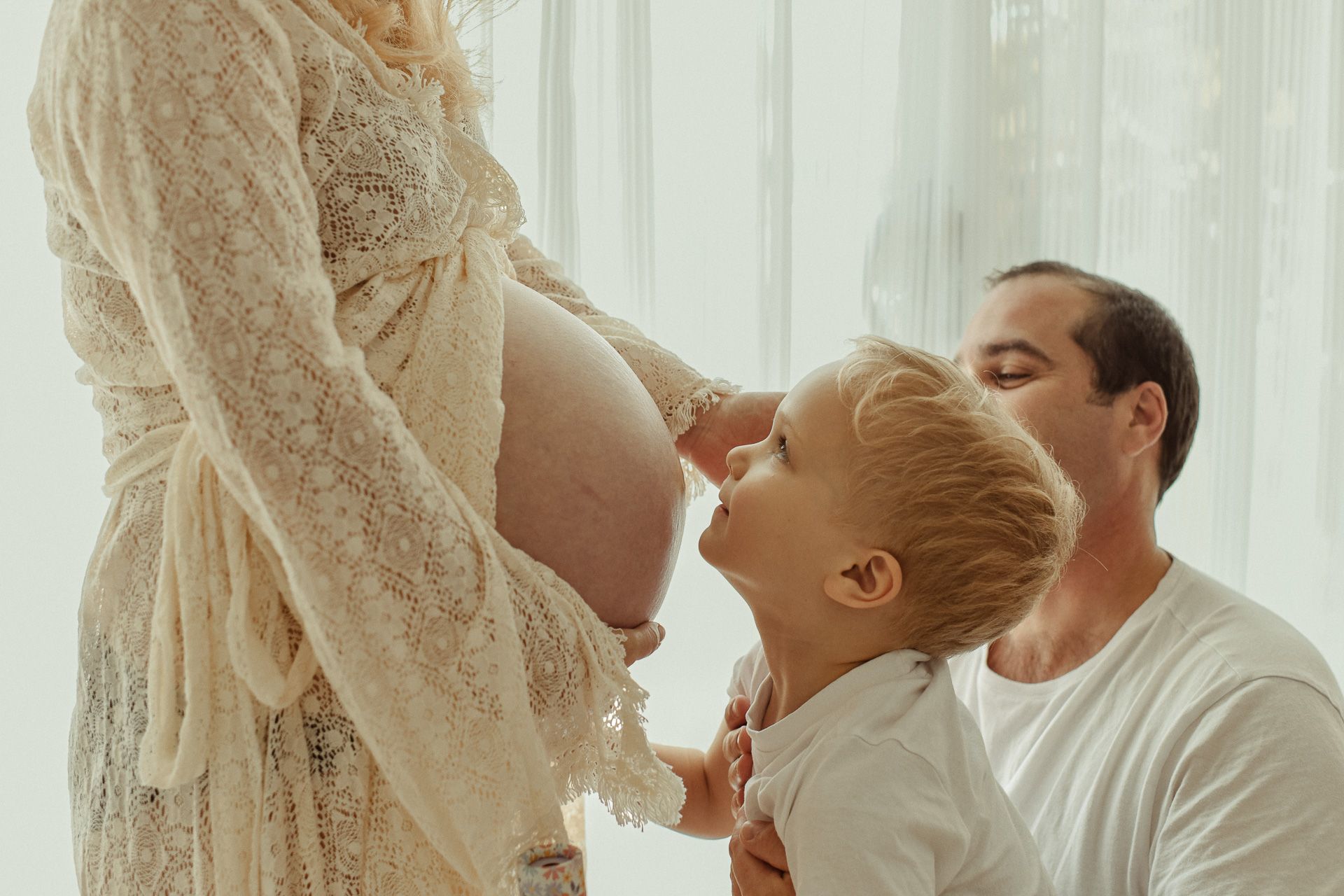 A touching maternity family shoot in a newborn studio, with a young child touching his mother's pregnant belly