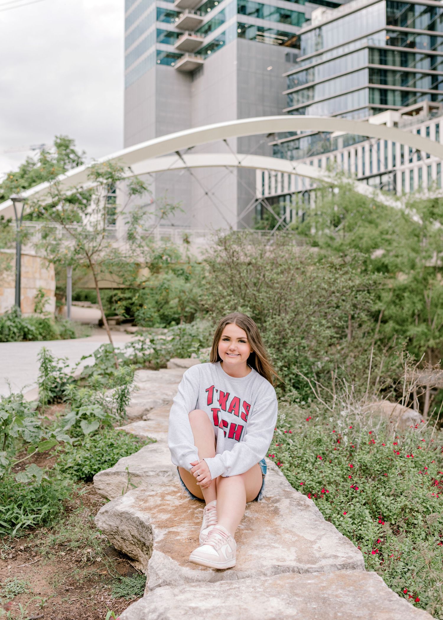 Student in Texas Tech sweatshirt posed on stone wall with modern architecture backdrop.