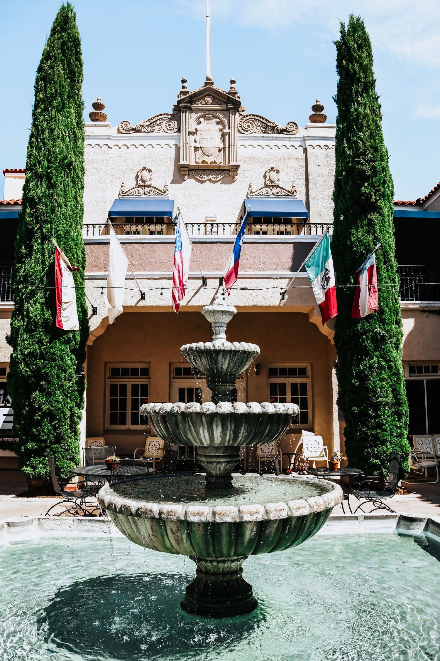 Ornate fountain with cypress trees at historic building entrance.