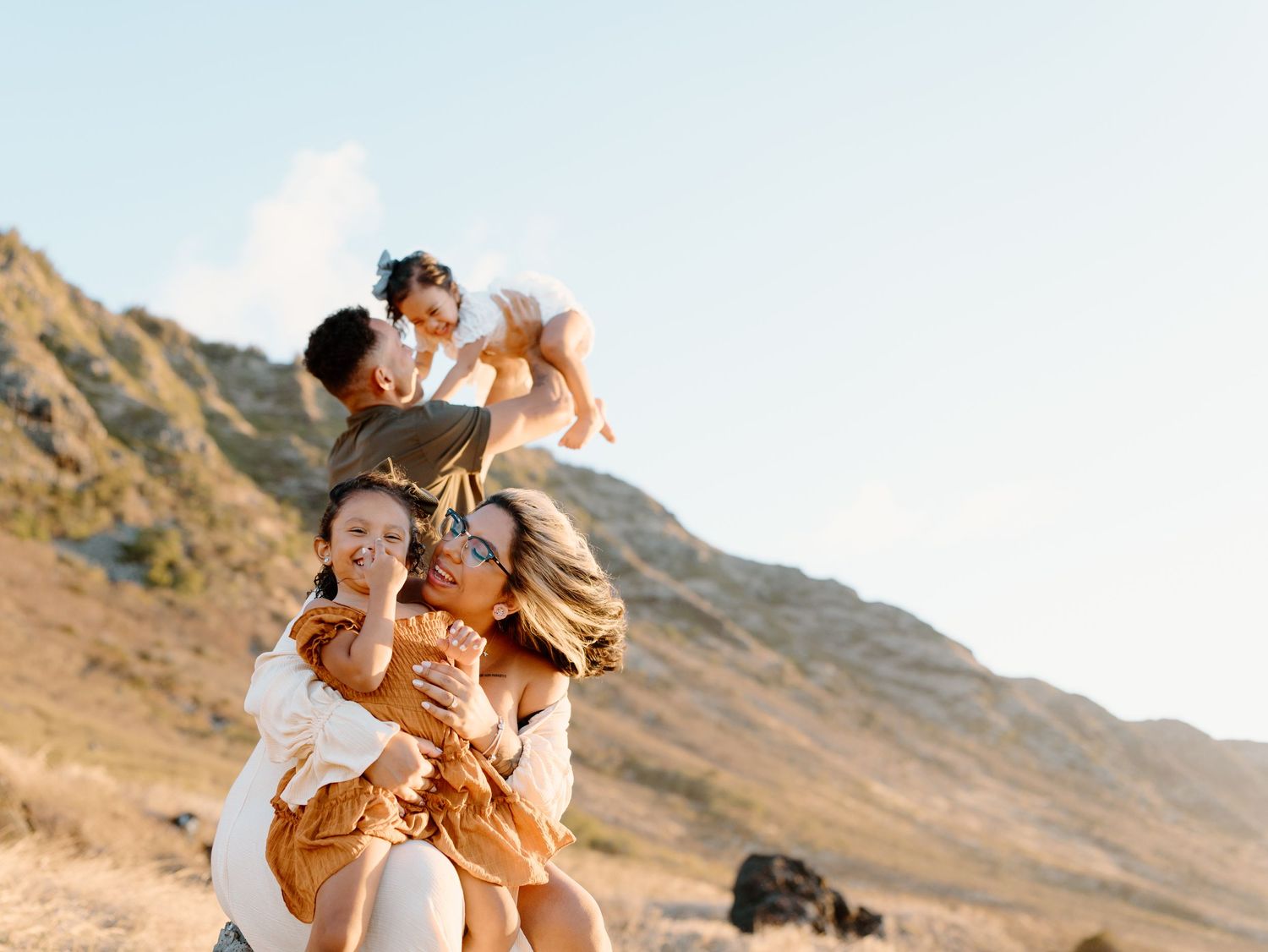 A family photoshoot by Moments With Kell with a mountain backdrop on Oahu in Hawaii with parents and laughing children