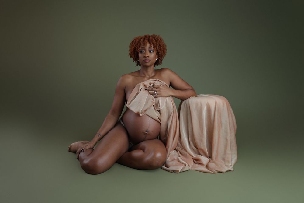 Elegant studio maternity portrait with soft lighting and champagne-colored fabric draping.