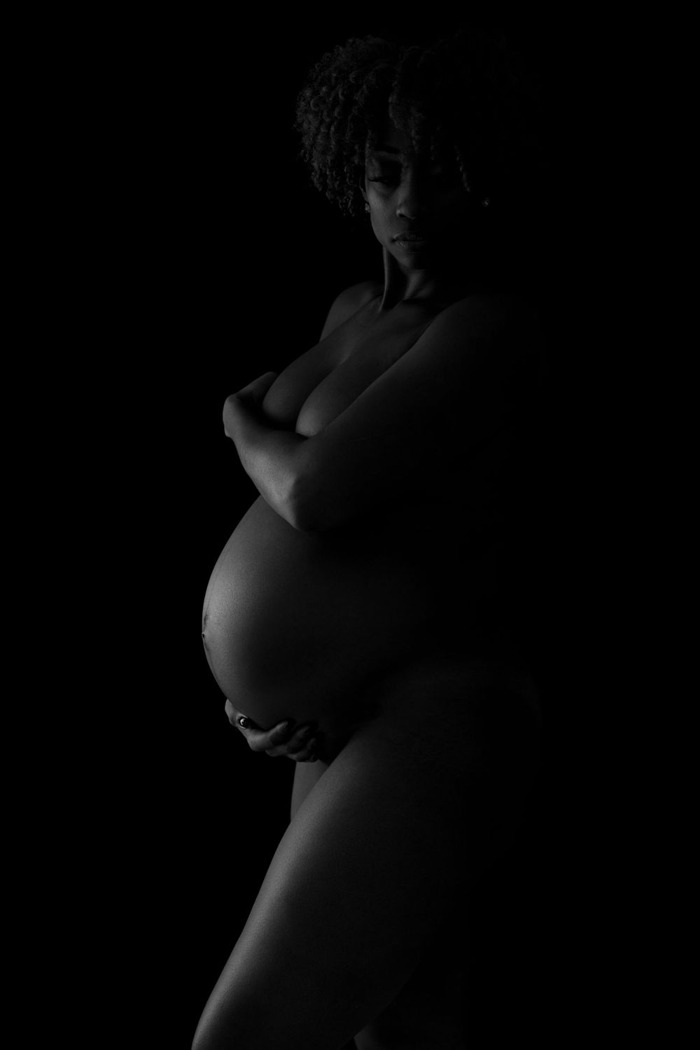 Dramatic black and white maternity silhouette highlighting a pregnant belly against a dark background.