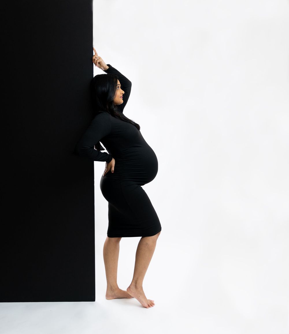 Artistic maternity silhouette in black dress against dramatic black and white background.