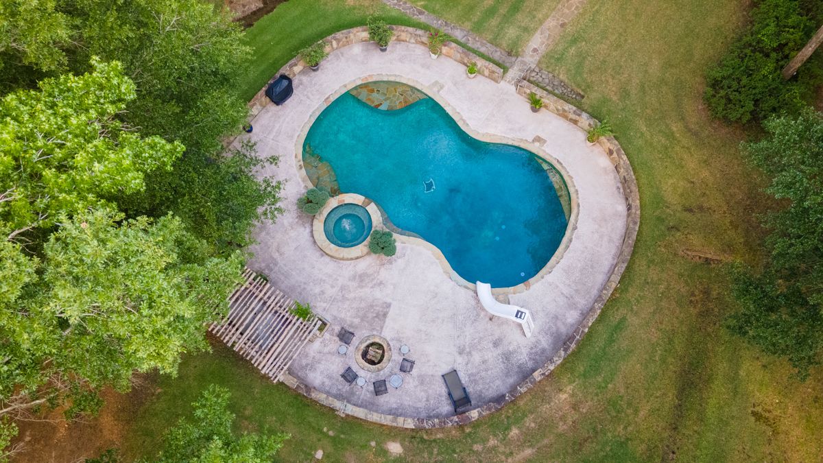 Aerial view of a freeform swimming pool with spa surrounded by concrete deck in landscaped backyard.
