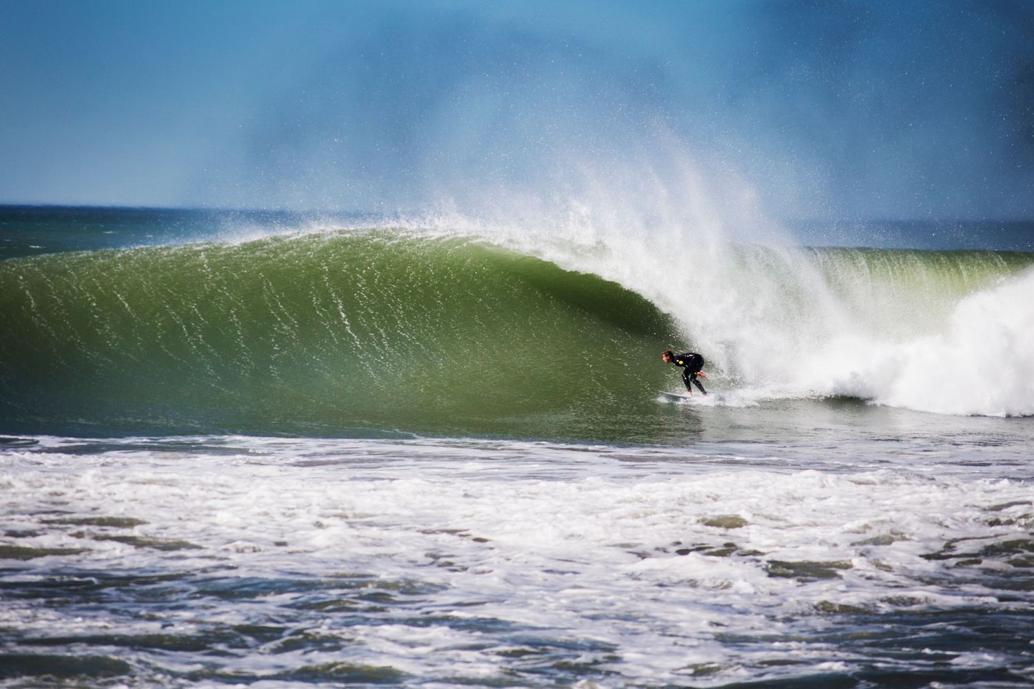 Large green wave breaking with spray in the ocean during high surf conditions.
