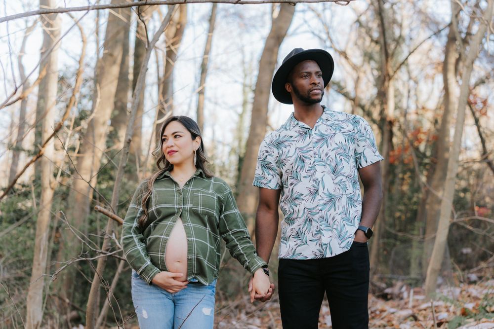 Couple in casual attire holding hands during forest maternity photoshoot.