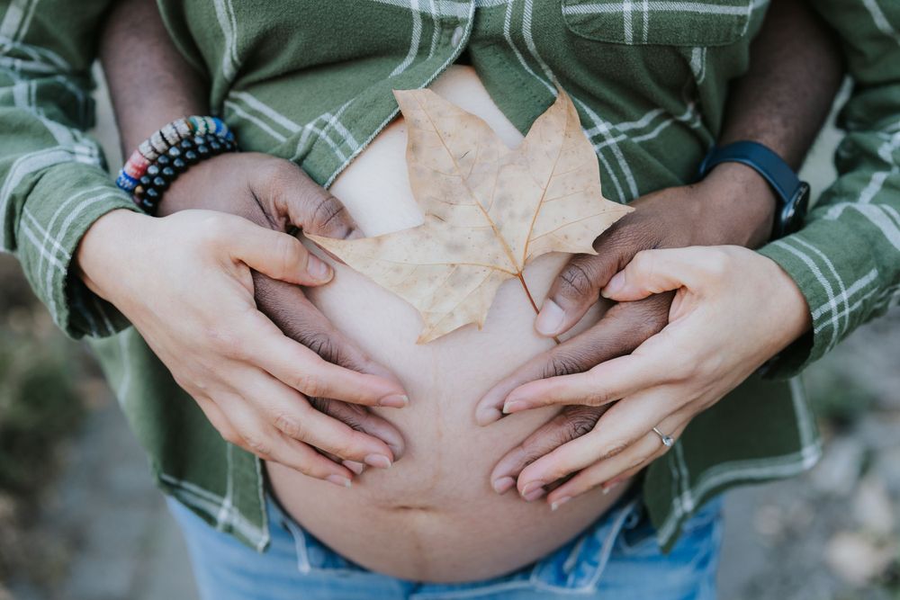 Close-up shot of hands cradling pregnant belly in plaid shirt.