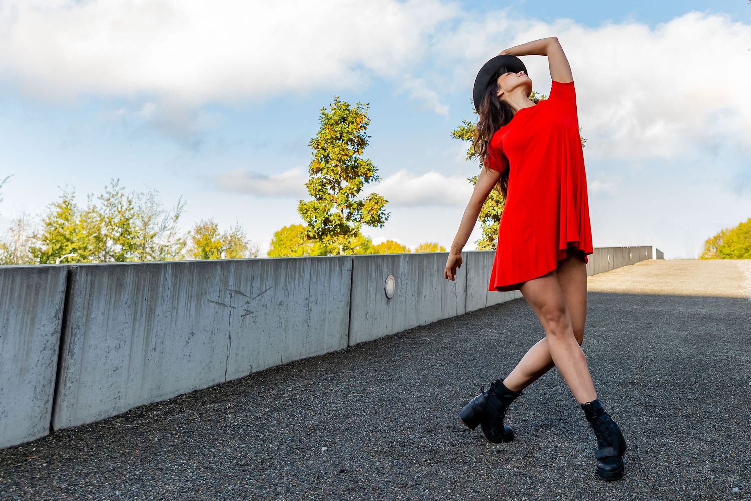 Dancer wearing a red dress and black hat, strikes a pose at the Seattle Sculpture Park during dance photo shoot.