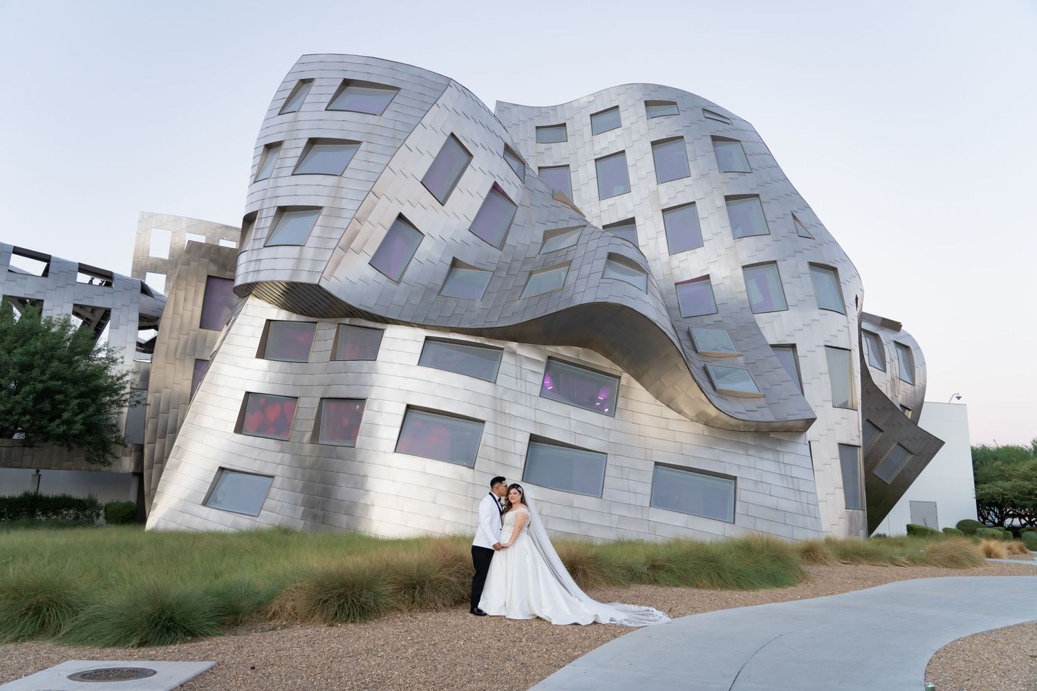 Wedding couple poses in front of a striking modern deconstructivist building with curved metallic facades.