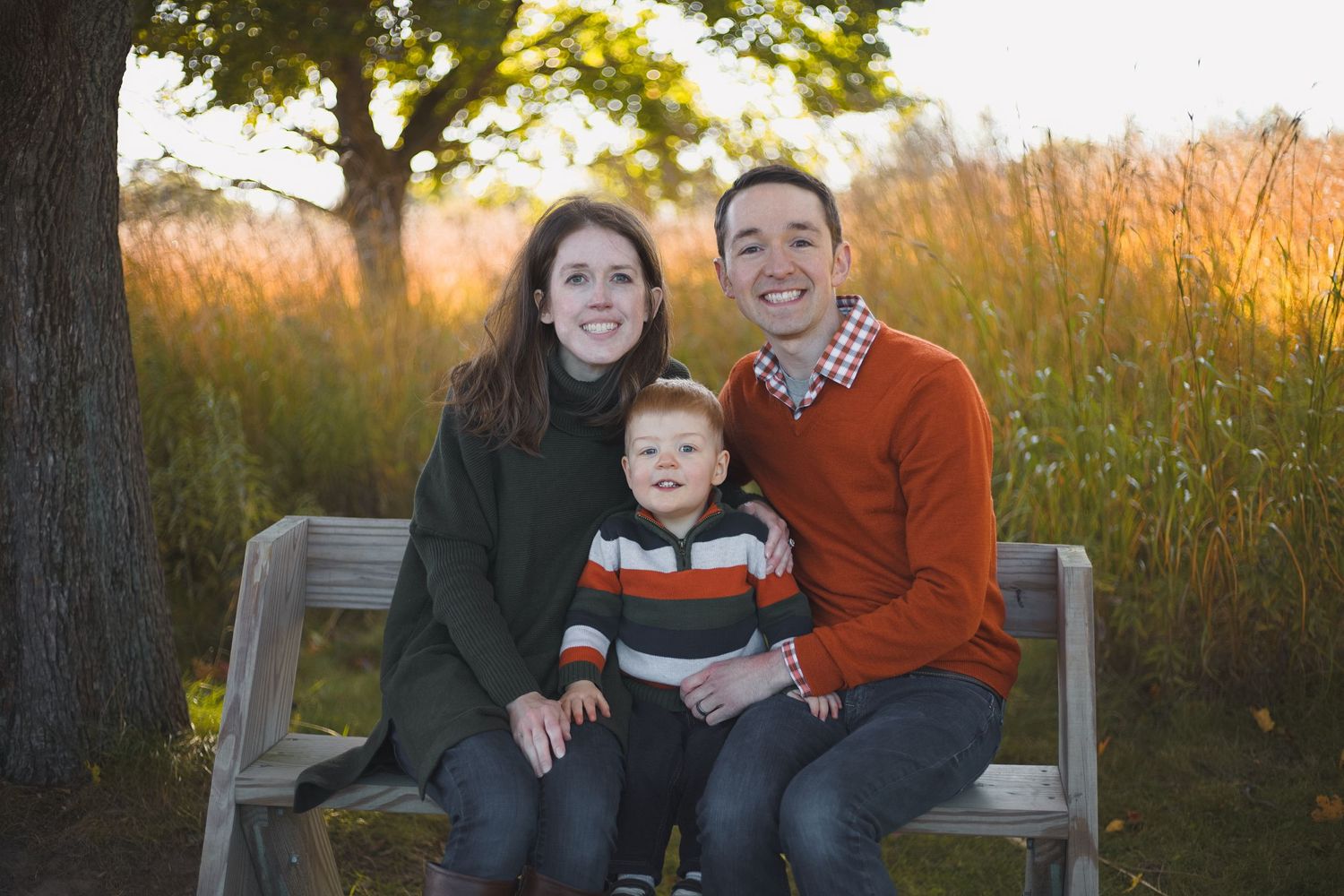 parents sitting on bench with toddler between them wearing fall colors