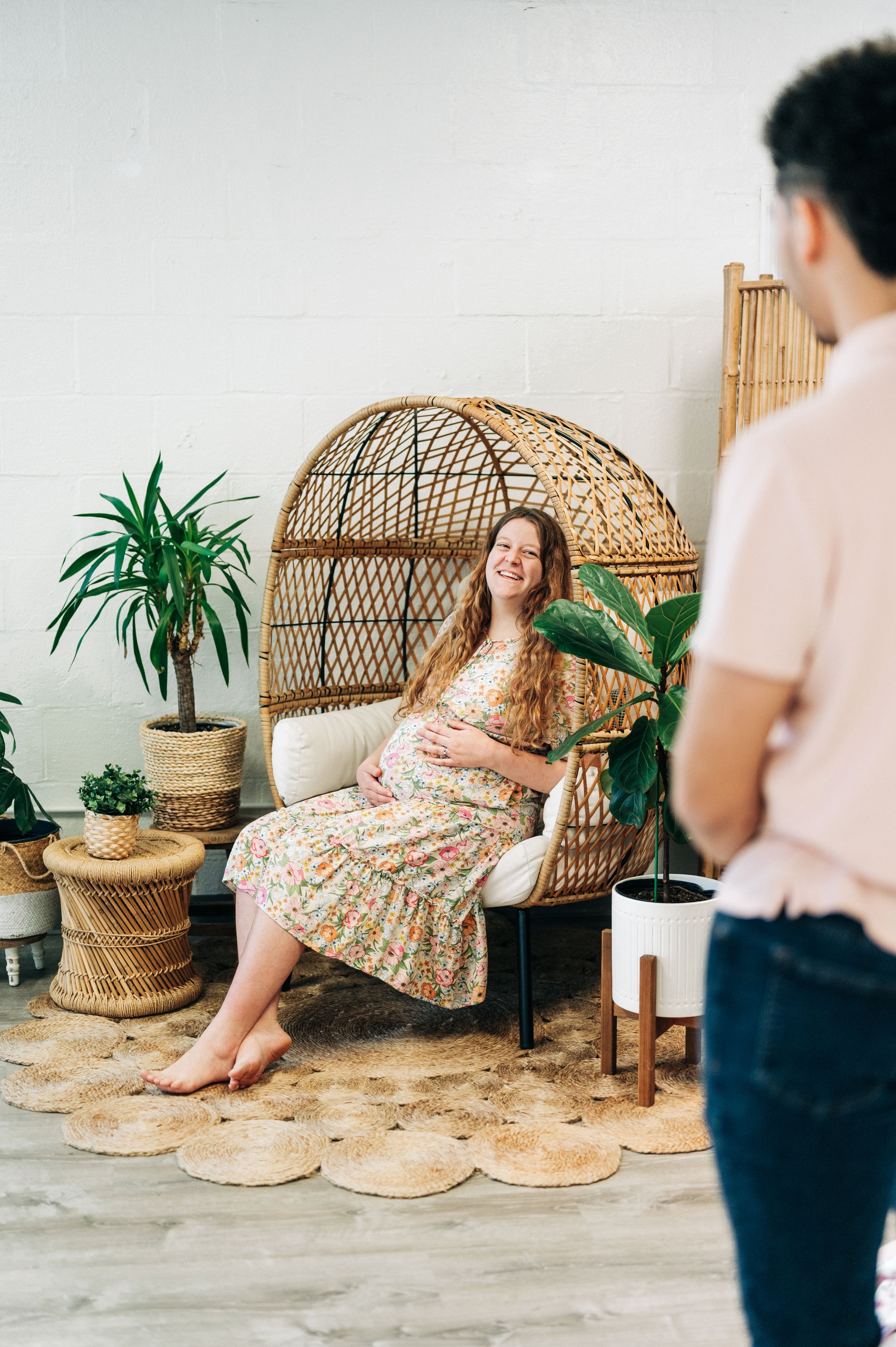 Maternity photoshoot in boho setting with wicker peacock chair and indoor plants.